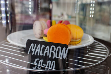 Macaroons on showcase in cafe. Macaron cake with price tag. Sweet food concept. Morning dessert. Orange macaron on plate in marketplace. Dessert assortment. French biscuit. - 757429771