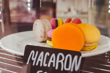 Macaroons on showcase in cafe. Macaron cake with price tag. Sweet food concept. Morning dessert. Orange macaron on plate in marketplace. Dessert assortment. French biscuit. - 757429785