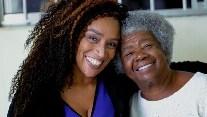 Happy portrait of adult African American daughter with arm around senior elderly gray-hair 80s...