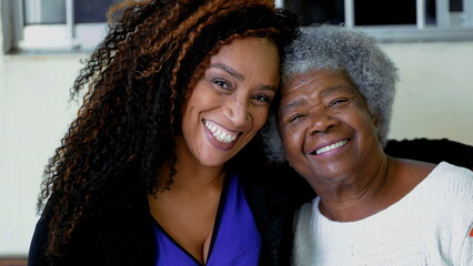 Happy portrait of adult African American daughter with arm around senior elderly gray-hair 80s...