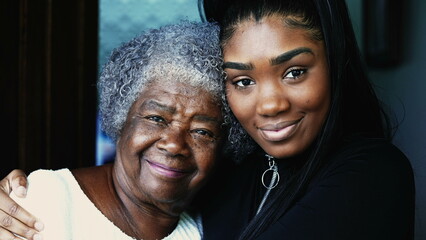 Happy portrait of young African American granddaughter with arm around her grandmother posing for...