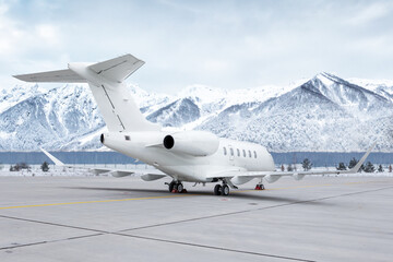 White luxury corporate aircraft at the airport apron on the background of high picturesque snow...