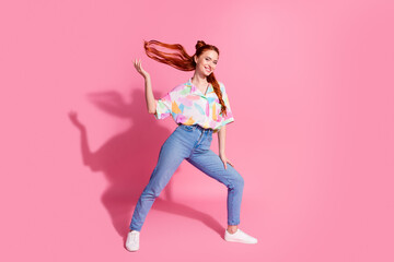 Full length photo of gorgeous optimistic woman wear print shirt jeans throwing up readhair tails isolated on pink color background