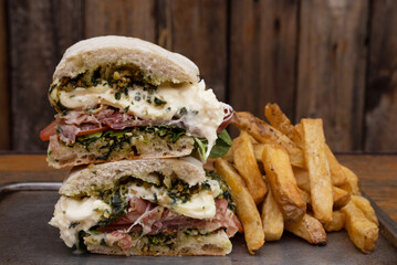Closeup view of a slice din half gourmet sandwich with layers of ciabatta bread, prosciutto ham,...