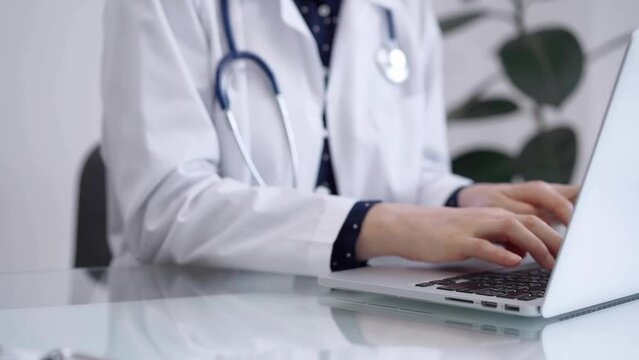 Doctor woman is working with laptop computer at the glass table in clinic. Physician is typing medical information or giving advices online. Medicine and pharmacy