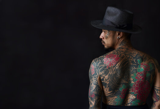 Back view of a man with black hat. Traditional yakuza member with his body entirely tattooed. With copy space for text. Gang member of the traditional Japanese mafia.