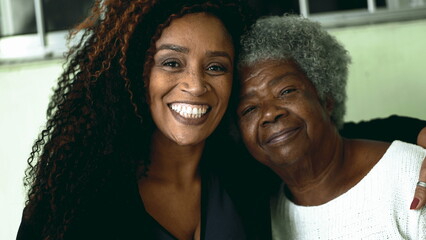 Tender loving moment of African American adult daughter kissing elderly 80s senior mother in the forehead and posing close-up faces smiling at camera - obrazy, fototapety, plakaty