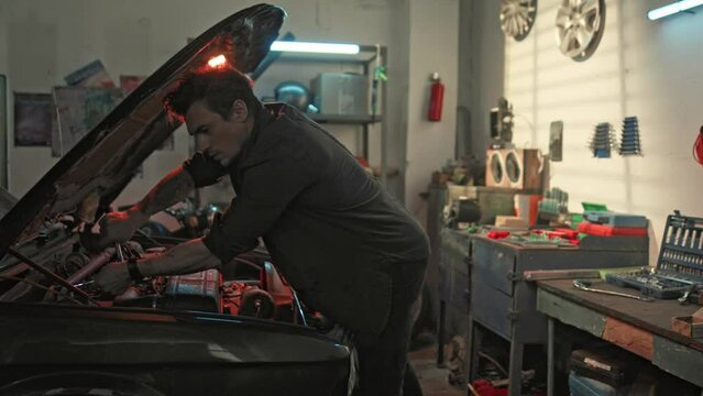Car service, repair, maintenance and people concept. Auto mechanic working in township workshop, looking at open car engine, checking if something is broken. Man with wrench working at garage.
