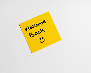 Inscription Welcome Back on the sticky note with red color pen on the office wooden desk. Praise from colleagues or boss. Positive compliment concept.