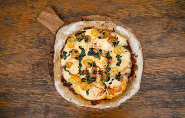 Pizza with mozzarella and provolone cheese, garlic and cherry tomatoes on the restaurant wooden table
