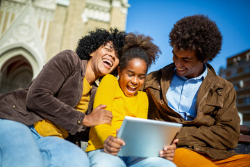 Family sitting on bench, relaxing using digital tablet, shopping online.