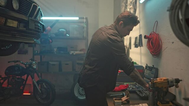 Portrait of handsome male auto mechanic in workshop. Young man working in home garage. Adult man, auto mechanic, finishes working in car workshop and puts all necessary tools in case.