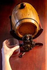 Left hand of person holding a glass of liquor in front of a Barrel with Padlock and key