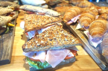 Triangular multigrain sandwiches with ham and tomato on a wooden board.