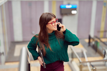 Fototapeta premium busy young professional woman talking on the cell phone leaving the subway