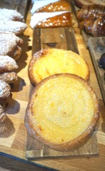 Golden custard tarts sprinkled with powdered sugar on a wooden display.