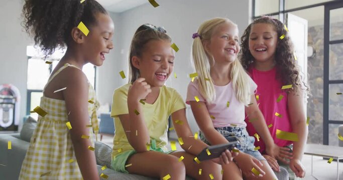 Animation of gold confetti over happy diverse schoolgirls using smartphone and laughing in classroom