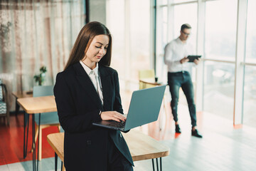 Portrait of a modern business woman with a laptop in the office. A business woman in a black classic suit who works online in the office