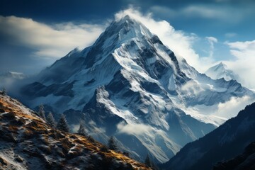 Snowy mountain shrouded in clouds with blue sky in the background - obrazy, fototapety, plakaty