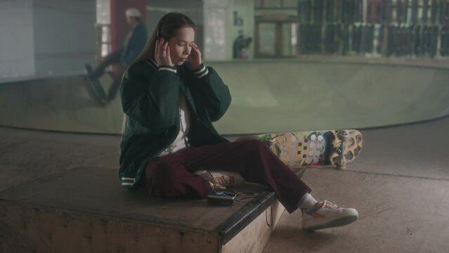 Young girl putting on headphones, turning on music on cassette tape player and going to ride skateboard at skatepark