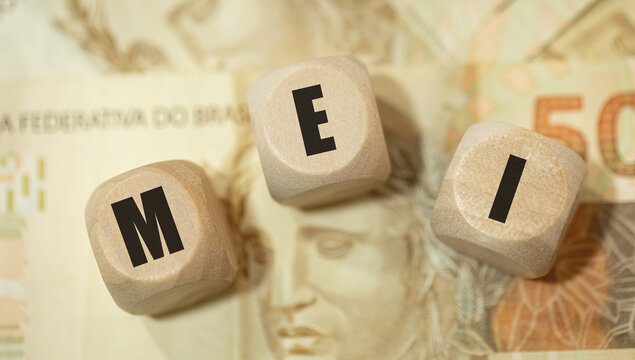 A abreviatura MEI para Microempreendedor Individual escrita em dados de madeira na linguagem Portugu&ecirc;s do Brasil. Notas de 50 Reais do Real Brasileiro na composi&ccedil;&atilde;o.