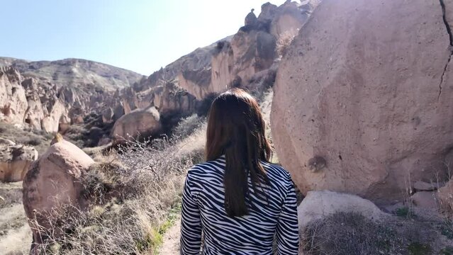 Solo female traveler walks by herself and enjoys the landscape of the valley filled with ancient settlements and fairy chimneys in Cappadocia.