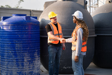 Worker engineer African woman hand shake with caucasian worker and water tank background at...