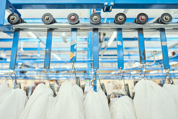 A metal roller rail in a textile factory industrial setting. Metal oil hangers on metal rollers....