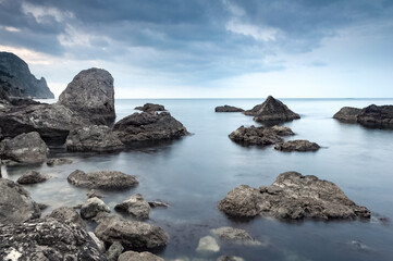 Calm sea. Summer morning. The clouds is reflecting on the water. Landscape with gray and brown stones in the sea. Monochrome scene. 
