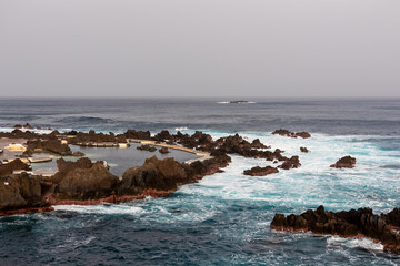 Natural lava pools with sunset view of volcanic rock formation Ilheu Mole in coastal town Porto Moniz, Madeira island, Portugal, Europe. Rugged coastline of Atlantic Ocean. Waves smashing shoreline