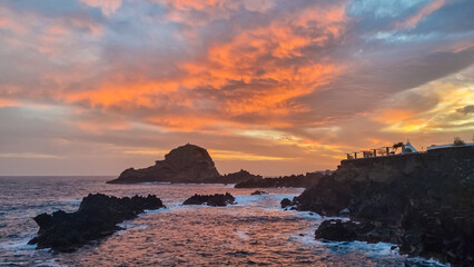 Panoramic sunset view of volcanic rock formation Ilheu Mole in coastal town Porto Moniz, Madeira island, Portugal, Europe. Rugged coastline of majestic Atlantic Ocean. Waves smashing against shoreline