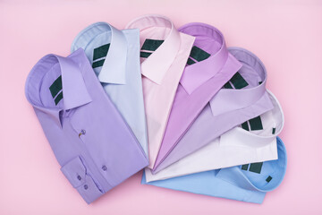 Multi-colored folded fanned men's shirts on pink background, top view