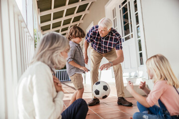Grandparents and grandchildren having fun with a soccer ball on house porch