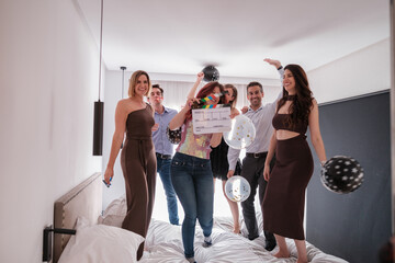 Group of young people jumping on the bed at a celebration party together. Concept: fun, happiness