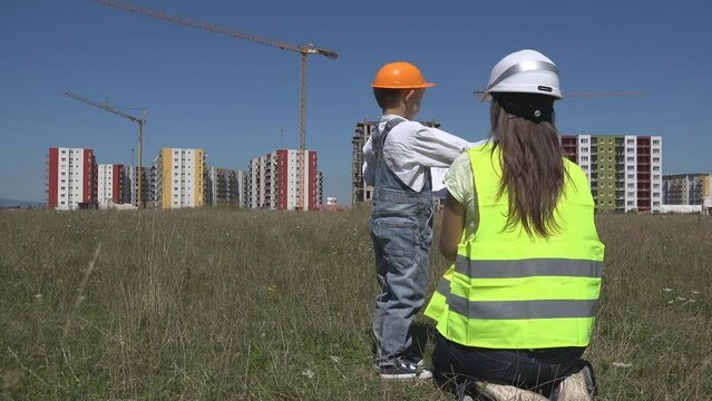 Mother and son with helmets watch the building plan near construction site