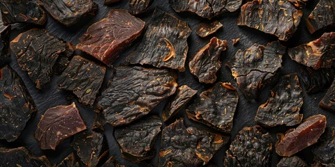 Schilderijen op glas Close up of dried meat on black background, textured jerky snack, traditional cured meat for protein lovers © SHOTPRIME STUDIO