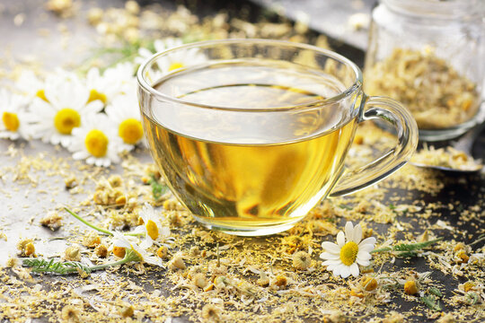 Chamomile herbal tea in a glass cup with flowers on black background, closeup, winter cold healing drink, natural medicine and naturopathy concept