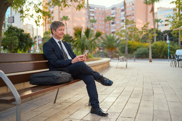 Man sitting on a bench typing on a mobile phone