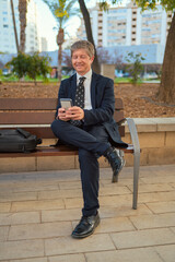 Obraz premium Man sitting on a bench typing on a mobile phone