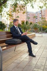 Man sitting on a bench typing on a mobile phone