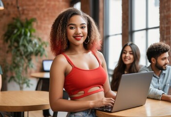 A confident woman stands with her laptop in a collaborative office space. Her red top and bright smile suggest enthusiasm and professionalism.