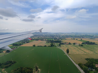 Airplane wing flying at low altitude over fields and mountains on the horizon, Emilia Romagna ITALY