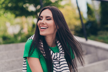 Photo of positive dreamy girl dressed green top sitting stairs enjoying sunshine smiling outdoors urban town park