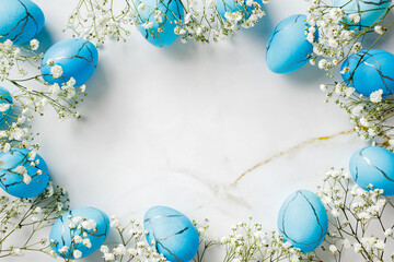 Frame of blue Easter eggs with elegant flowers on marble background. Flat lay, top view, copy space.