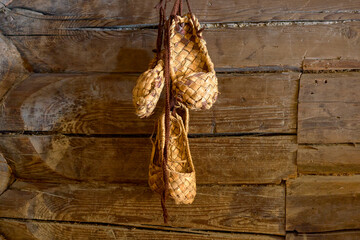 Woven bast shoes hang on the wall in the sun. Rustic vintage shoes.