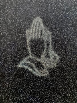 Outline of prayer hands on a dark, textured background