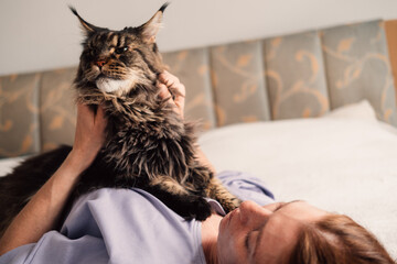 A serene moment as a woman lies back on a bed, stroking a majestic Maine Coon cat