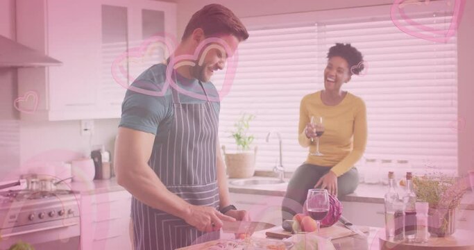 Animation of hearts over diverse couple cooking together and drinking wine in kitchen at home