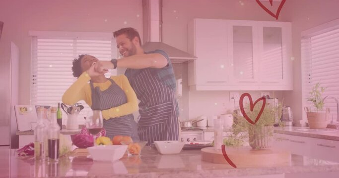 Animation of hearts over diverse couple dancing in kitchen at home