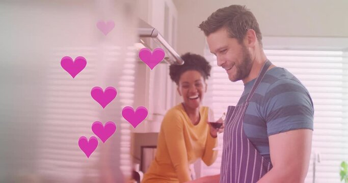 Animation of hearts over diverse couple cooking together and drinking wine in kitchen at home